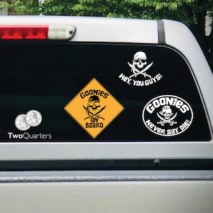 May include: Three Goonies themed car decals. The first decal is a yellow diamond with the words "Goonies On Board" and a skull and crossbones. The second decal is a circle with the words "Goonies Never Say Die!" and a skull and crossbones. The third decal is a skull and crossbones with the words "Hey You Guys!"
