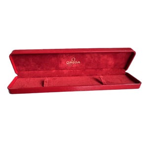 May include: Open red watch box with a plush interior. The box is rectangular and has a hinged lid. The Omega logo is visible inside the lid. The box is designed to hold a watch.