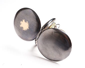 May include: An open, antique pocket watch with a silver-tone case and a gold-colored accent. The watch case has a textured, striped pattern. The open face reveals the inner workings of the watch. The watch is set against a white background.