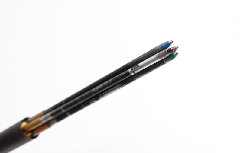 Puede incluir: Primer plano de varios recambios de bol&iacute;grafo negros con puntas de tinta azul, roja y verde. Los recambios est&aacute;n angulados hacia la esquina superior derecha sobre un fondo blanco. Los bol&iacute;grafos est&aacute;n en un portal&aacute;pices negro.