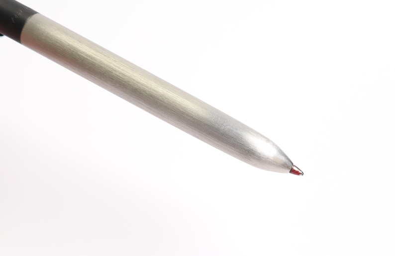 Puede incluir: Primer plano de un bol&iacute;grafo plateado con la parte superior negra. La punta del bol&iacute;grafo es de color rojo oscuro. El bol&iacute;grafo est&aacute; en &aacute;ngulo diagonal sobre un fondo blanco.