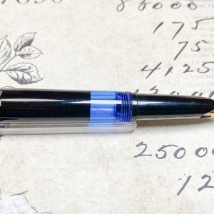 K&ouml;nnte beinhalten: Ein schwarzer und goldener F&uuml;llfederhalter mit einer blauen Tintenpatrone. Der F&uuml;ller hat eine goldene Verzierung und die Worte "V16 EF" sind auf der Seite eingraviert.