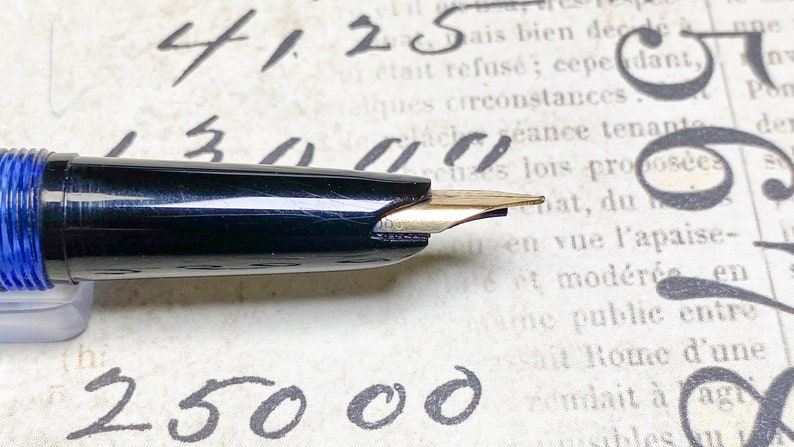 K&ouml;nnte beinhalten: Ein schwarzer und blauer F&uuml;llfederhalter mit einer goldenen Feder. Der Stift liegt auf einem Blatt Papier mit handschriftlichem Text.