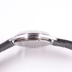 May include: A silver wristwatch with a black leather band. The watch is on a white background.