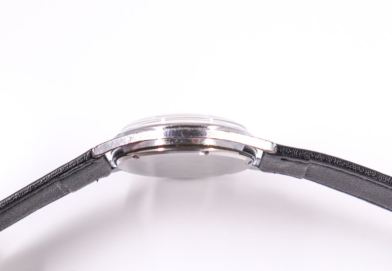 May include: A silver wristwatch with a black leather band. The watch is on a white background.