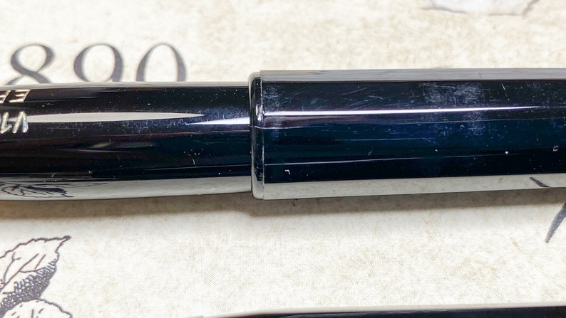 K&ouml;nnte beinhalten: Ein schwarzer F&uuml;llfederhalter mit silberner Klammer und schwarzer Kappe. Der Stift ist geschlossen und die Kappe ist auf dem Stift.