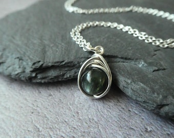 Può includere: Una collana con catena d'argento con un ciondolo di pietra preziosa verde scuro. Il ciondolo è avvolto in filo d'argento.