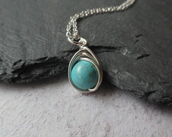 May include: A silver chain necklace with a turquoise gemstone pendant. The pendant is wrapped in silver wire.