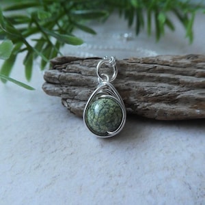 May include: A silver chain necklace with a green and white stone pendant. The stone is wrapped in silver wire and has a teardrop shape.
