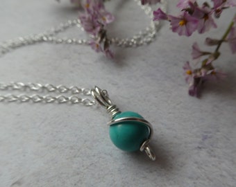 May include: A turquoise gemstone pendant necklace with a silver chain. The gemstone is wrapped in silver wire.