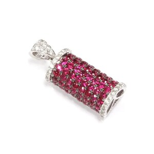 Pode incluir: Um pingente de ouro branco com formato cilíndrico, incrustado com rubis vermelhos e diamantes brancos.