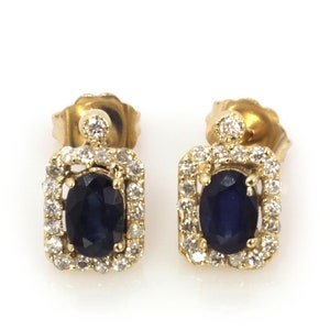 Pode incluir: Um par de brincos de ouro com um safira azul e um halo de diamantes. Os brincos são de forma oval e têm uma moldura quadrada.