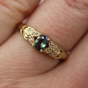 May include: A gold ring with a green oval gemstone surrounded by smaller white gemstones. The ring has a delicate, leaf-like design.