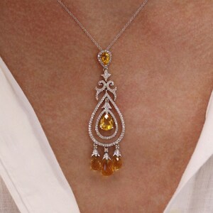 May include: A delicate gold pendant necklace with a teardrop-shaped center stone and smaller teardrop stones hanging from the bottom. The pendant is set with clear and yellow gemstones.