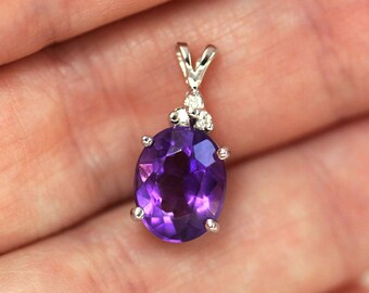 May include: A silver pendant featuring a large oval amethyst gemstone with a cluster of smaller diamonds at the top.