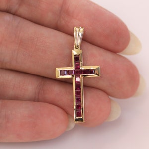 Puede incluir: Un colgante de cruz de oro con piedras preciosas cuadradas rojas engastadas en la cruz.