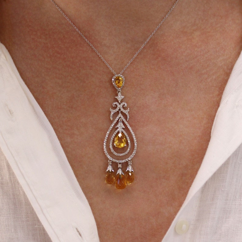 May include: A delicate gold pendant necklace with a teardrop-shaped center stone and smaller teardrop stones hanging from the bottom. The pendant is set with clear and yellow gemstones.