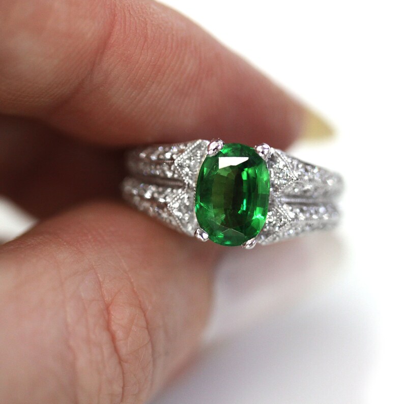 May include: A silver ring featuring a large, oval green gemstone surrounded by smaller diamonds. The ring is set in a delicate, intricate design.
