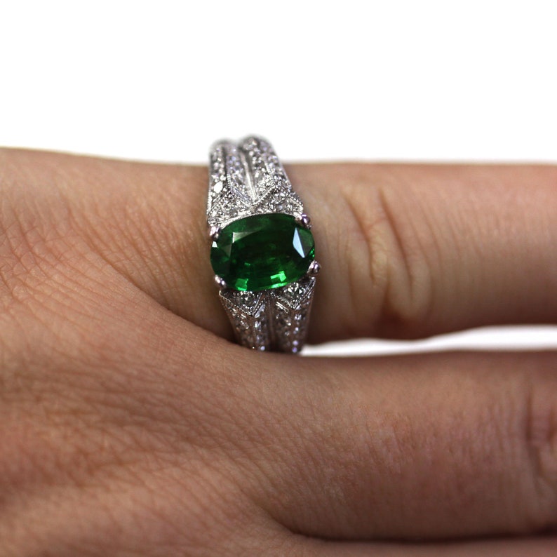 May include: A silver ring featuring a large oval green gemstone surrounded by smaller diamonds.