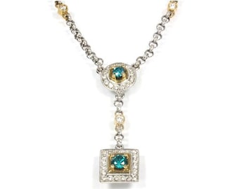 Op de afbeelding: Een zilveren en gouden ketting met een vierkante en ronde hanger met blauwe edelstenen omringd door kleinere diamanten.