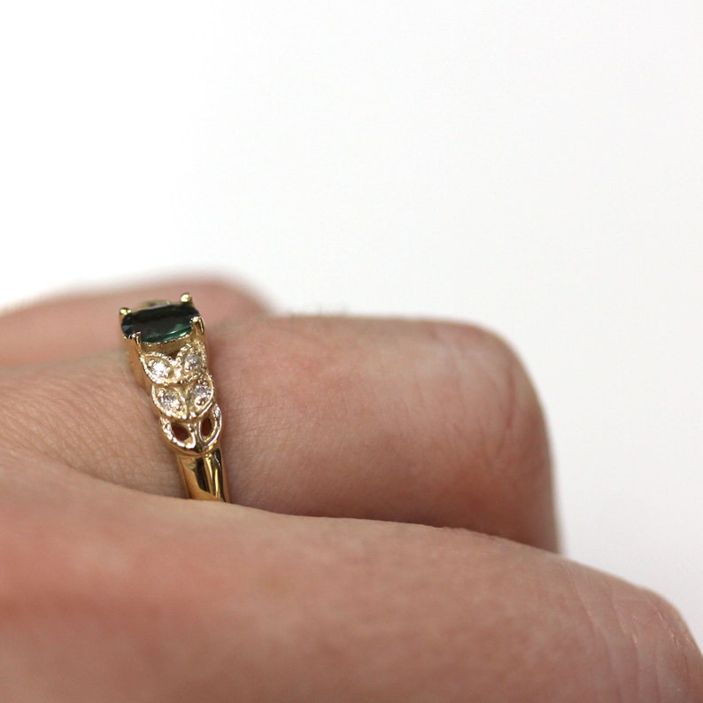 May include: A gold ring with a green gemstone and small white gemstones set in a leaf design.