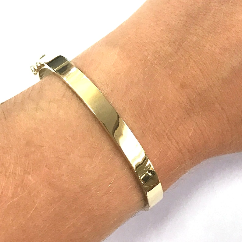 以下が含まれることがあります： 滑らかで磨かれた仕上げのゴールドのバングルブレスレット。ブレスレットは開いており、ヒンジ付きの留め具が付いています。