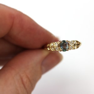 May include: A gold ring with a green gemstone surrounded by small diamonds. The ring has a leaf-like design.