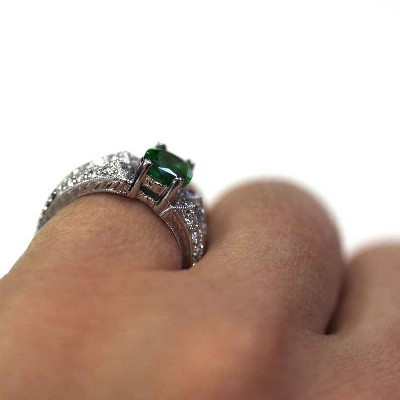 May include: A silver ring featuring a large green gemstone surrounded by smaller clear gemstones.
