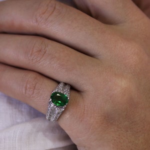 May include: A silver ring featuring a large, oval green gemstone surrounded by smaller diamonds.