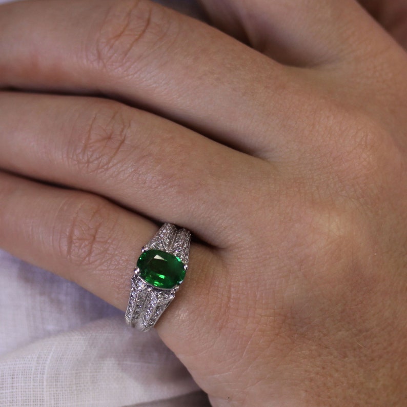 May include: A silver ring featuring a large, oval green gemstone surrounded by smaller diamonds.