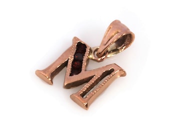 May include: A gold pendant charm in the shape of the letter "M" with red gemstones set into the letter.
