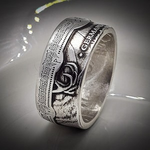 Op de afbeelding: Een zilveren ring gemaakt van een Duitse 5 Mark munt. De munt heeft een gestileerd beeld van een hert met gewei en de tekst "GERMAN 5 MARK" rond de rand.