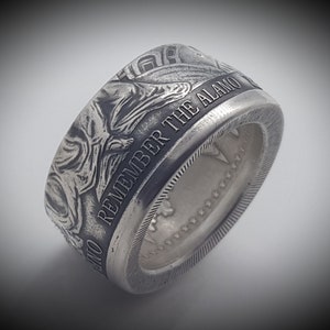 May include: A silver ring made from a US half dollar coin. The coin has been engraved with the words "Remember the Alamo" and a design of the Alamo.