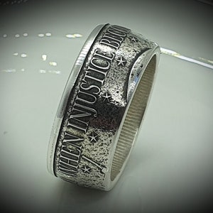 Pode incluir: Um anel de prata com as palavras "When Injustice Becomes Law" gravadas em torno da banda. O anel tem uma superfície texturizada e um design de estrela.