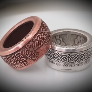 Könnte beinhalten: Zwei Ringe aus wiederverwendeten Münzen. Der Ring links ist aus Kupfer und zeigt ein keltisches Knotendesign und das Wort "Copper". Der Ring rechts ist aus Silber und zeigt ein keltisches Knotendesign und den Text "20c 666 Fine Silver".