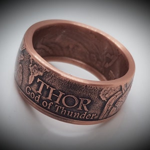 Könnte beinhalten: Ein kupferfarbener Ring mit einer strukturierten Oberfläche und den Worten "THOR Gott des Donners" auf der Seite eingraviert.
