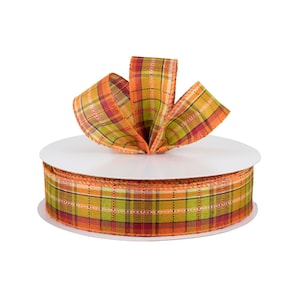 May include: A roll of orange, green, and red plaid ribbon with a bow on top. The ribbon is on a white spool.