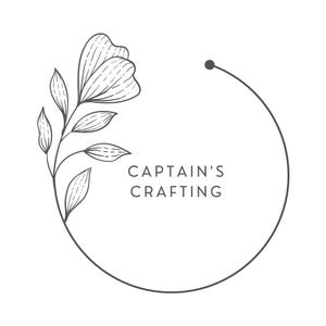 May include: A black and white line drawing of a floral wreath with the text "CAPTAIN'S CRAFTING" in the center.
