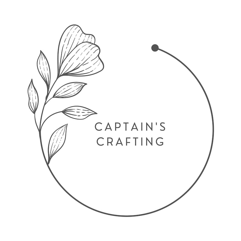 May include: A black and white line drawing of a floral wreath with the text "CAPTAIN'S CRAFTING" in the center.