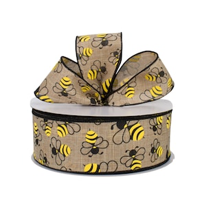 May include: A decorative ribbon roll featuring a repeating pattern of yellow and black bees on a tan background. The ribbon is made of a burlap-like material and is tied into a bow on top of the roll. The roll is approximately 4 inches in diameter.
