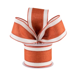 May include: A spool of decorative ribbon with a repeating pattern of orange and white stripes. The ribbon is made of a textured fabric and is arranged in a bow shape on top of the spool. The ribbon is suitable for crafts and gift wrapping.