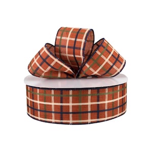 May include: A roll of 2.5 inch wide plaid ribbon with a rust, green, white, and navy blue color scheme. The ribbon is made of a woven fabric with a slightly textured surface.