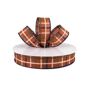 May include: A roll of orange, green, and white plaid ribbon with a navy blue edge. The ribbon is tied in a bow on a white surface.