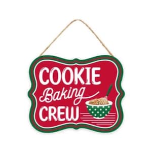 May include: A red, green, and white sign with the words "COOKIE BAKING CREW" in white script. The sign features a green and white polka-dot bowl with a whisk and baked goods. A jute rope is attached for hanging.