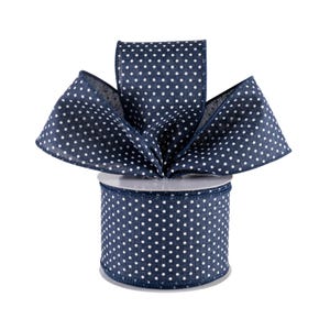 May include: A spool of navy blue ribbon featuring a repeating pattern of small white polka dots. The ribbon is wound around a cylindrical core, with a portion of the fabric folded and fanned out at the top to display the texture and pattern.