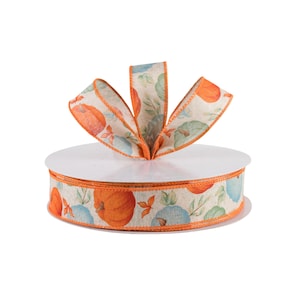 May include: A spool of orange and blue patterned ribbon with a pumpkin design. The ribbon is on a white spool and is ready to be used for crafting or decorating.