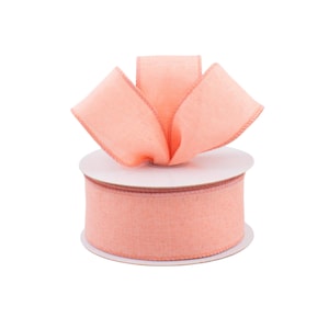 May include: A spool of peach-colored ribbon with a matching bow on top. The ribbon has a textured appearance and is displayed on a white background. The bow is made of the same ribbon material and is neatly arranged.