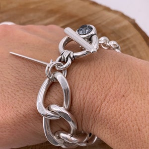 May include: A silver chunky chain bracelet with a toggle clasp featuring a dark gray gemstone.