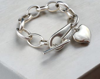 Pulsera gruesa artesanal bañada en plata con cierre de palanca y colgante de corazón.