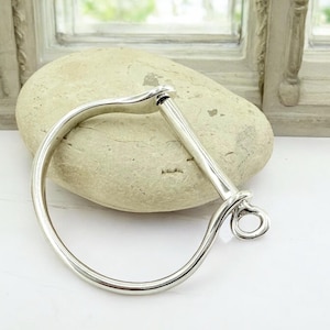 Könnte beinhalten: Ein silbernes Armreif-Armband mit einem einzigartigen, geschwungenen Design und einem Hakenverschluss.